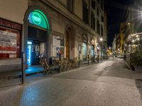 a street with benches sitting on the sidewalk and people walking down the street at night