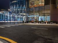 a street that has cars on it and people standing outside at a bus stop in the night