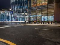 a street that has cars on it and people standing outside at a bus stop in the night