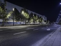 empty street lit up at night by street lamps and concrete pavement by curbed roadway