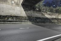 a empty street at night under the lights of the buildings, near an overpass