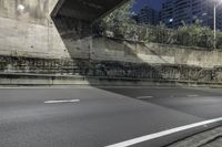 a empty street at night under the lights of the buildings, near an overpass