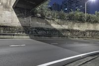 a empty street at night under the lights of the buildings, near an overpass