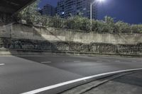 a empty street at night under the lights of the buildings, near an overpass