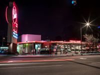 the exterior of a restaurant on an urban street at night with bright lights on it