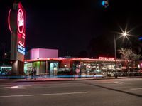 the exterior of a restaurant on an urban street at night with bright lights on it