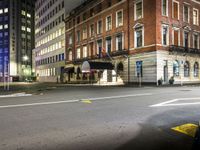 a deserted city street with a fire hydrant and tall buildings behind it at night