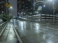 the street with no people is wet and has a light on at night in an urban area