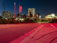 a red street is lit by lights in the dark with buildings in the background and flags in the foreground