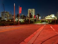 a red street is lit by lights in the dark with buildings in the background and flags in the foreground