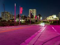 a red street is lit by lights in the dark with buildings in the background and flags in the foreground