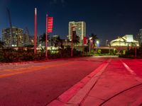 a red street is lit by lights in the dark with buildings in the background and flags in the foreground