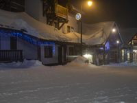 a snow covered street near some houses and lights in the air with one person walking under it