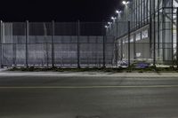 a street that has a fence and some street lights on it at night, in the city