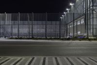 a street that has a fence and some street lights on it at night, in the city