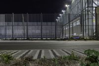 a street that has a fence and some street lights on it at night, in the city