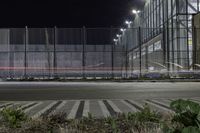 a street that has a fence and some street lights on it at night, in the city