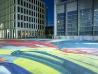 the view of the street with colorful carpet at night in the city park with modern buildings and a large window