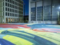 the view of the street with colorful carpet at night in the city park with modern buildings and a large window