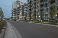 a street in front of an apartment complex with parking meters next to it, in the evening