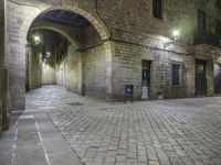 street lights shine brightly along an empty cobblestone courtyard and stone steps leading to two buildings