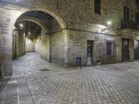 street lights shine brightly along an empty cobblestone courtyard and stone steps leading to two buildings