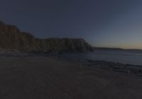 a bench that is in front of some rocks and water at sunset with the moon and trees