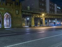 an empty street under a bridge at night time, with lights on and cars coming