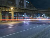 an empty street under a bridge at night time, with lights on and cars coming