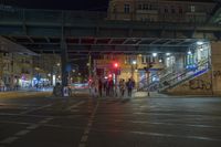 many people stand in a busy road in town at night on a bridge above them