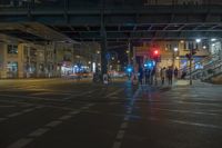 many people stand in a busy road in town at night on a bridge above them