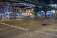 a street with some people crossing over the bridge at night time and several cars on the roadway below