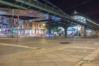 a street with some people crossing over the bridge at night time and several cars on the roadway below