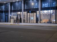 a bicycle parked on the sidewalk outside of an office building at night, along with two glass windows