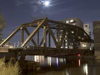 a train bridge crossing a river at night with the moon in the sky behind it