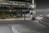 steps leading down to large building at night on sidewalk in dark courtyard area with glass railings