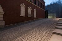 an empty brick driveway and stairs with red brick buildings at night in the background, with clouds in the sky