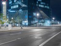 an empty street near a very tall glass building at night, on a busy road