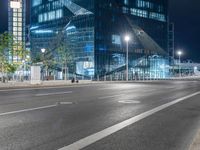 an empty street near a very tall glass building at night, on a busy road