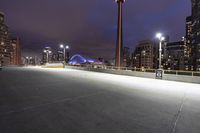 an empty parking lot with city lights on it at night time with blue sky in the background