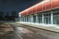 an empty parking lot with a sign pointing at a red and yellow building at night