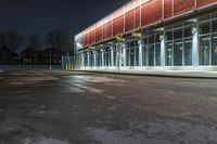 an empty parking lot with a sign pointing at a red and yellow building at night