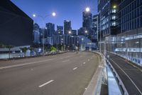 an empty road in front of some tall buildings at night with the lights on and street lights lit up