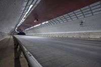 a tunnel with traffic traveling along the side of it and in between the ceiling, there is an empty road and lights on