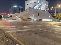 a large concrete building is sitting by a street corner at night, with red traffic lights