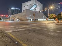 a large concrete building is sitting by a street corner at night, with red traffic lights