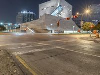 a large concrete building is sitting by a street corner at night, with red traffic lights