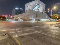 a large concrete building is sitting by a street corner at night, with red traffic lights