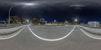 an empty street with lights and buildings in the background at night time with a curved road