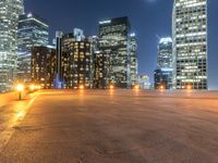 an empty parking lot with skyscrapers in the background at nighttime in an urban area